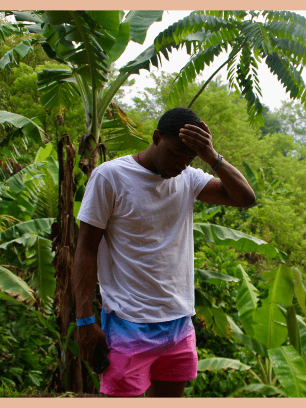 black male traveler surrounded by greenery holding his palm to his head after making some sort of travel mistake