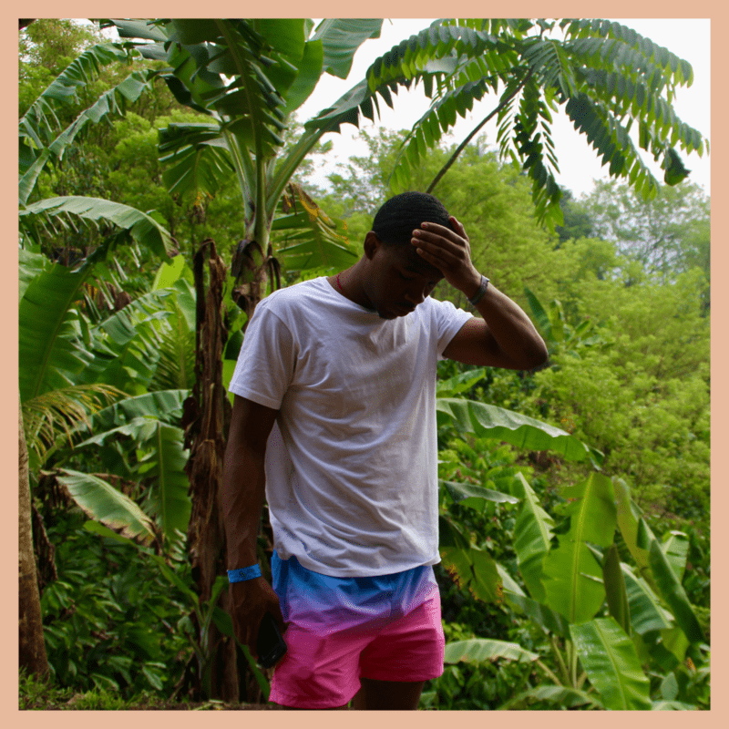 black male traveler surrounded by greenery holding his palm to his head after making some sort of travel mistake
