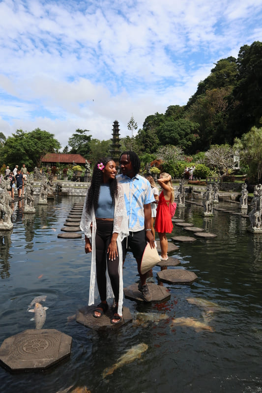black budget travel couple smiling at eachother posing on the pillar path in the water at tirta gangga