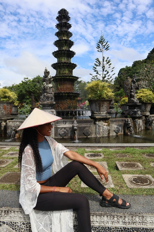 black budget traveler sitting alsong tirta gangga smiling out at the view of fountains and greenery in bali