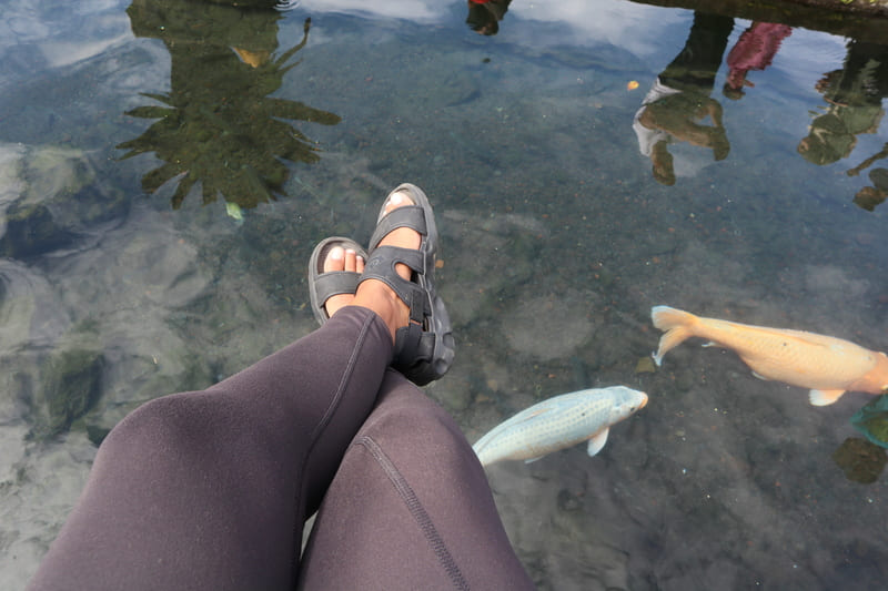 black woman with legs crossed hanging over the large coi fish swimming in the water.